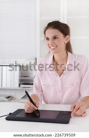 Young female graphic artist sitting at des working with tablet.