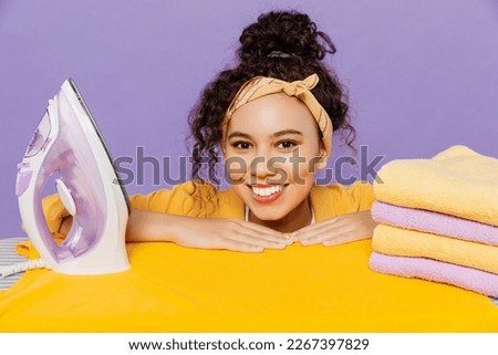Close up young housekeeper housewife woman wear yellow shirt white t-shirt tidy up ironing clean clothes on board isolated on plain pastel light purple background studio Housework housekeeping concept