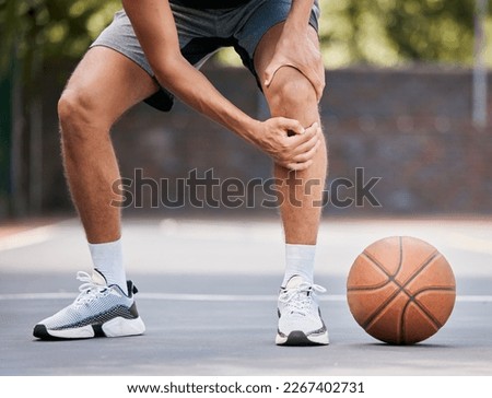 Pain, basketball and man with knee injury standing on outdoor court, holding leg. Sports, fitness and athlete with joint pain, injured and hurt in training, workout and game on basketball court