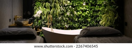 Bath in modern beauty salon, luxury bathroom interior in spa with vertical garden. Green plants wall, massage beds and bathtub in hotel. Concept of nature, landscaping, water, wellness, room. Royalty-Free Stock Photo #2267406545