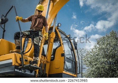 Professional Heavy Duty Machinery Operator Standing on Excavator Machine. Construction Industry Theme. Royalty-Free Stock Photo #2267413985
