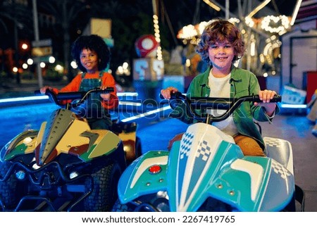 An African-American girl and a cute Caucasian boy riding a car ride together in the evening at a carousel and amusement park. Royalty-Free Stock Photo #2267419765