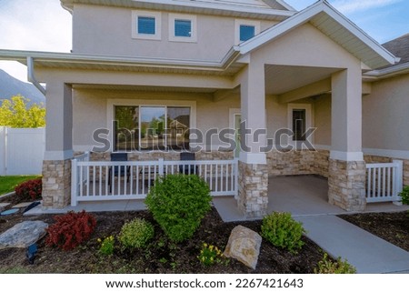 Utah- Two-storey house with square windows above the porch with chairs and white railings. Entrance of a house with plants near the railings at the front of the chairs near the window beside the door. Royalty-Free Stock Photo #2267421643