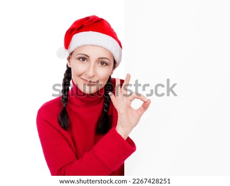 Girl in Santa Hat making OK sign from behind blank advertising sign billboard  isolated on a white background. Sale concept.