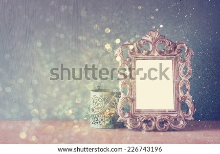 low key image of vintage antique classical frame and Burning candle on wooden table and glitter lights background .