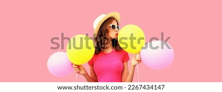 Summer colorful image of cute young woman kissing yellow pink balloons wearing straw hat on pink background