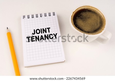 Business concept. On a white surface, a cup of coffee, a pencil and a notepad with the inscription - JOINT TENANCY