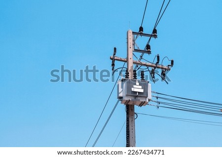 AC high-voltage power transformer on electric pole with wires on a background of blue sky, high voltage transmission line.                             Royalty-Free Stock Photo #2267434771