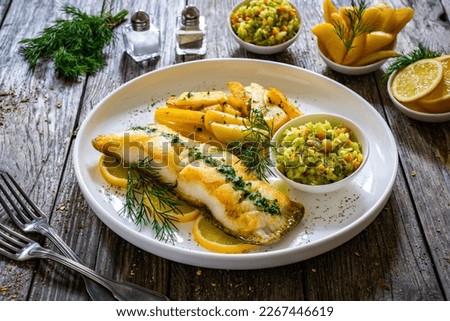 Fish dish - fried halibut with French fries and cabbage salad on wooden table 