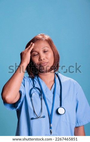Tired nurse having migraine while working at medical expertise during checkup visit appointment, portrait. Depressed sick assistant suffering from headache. Health care service and concept