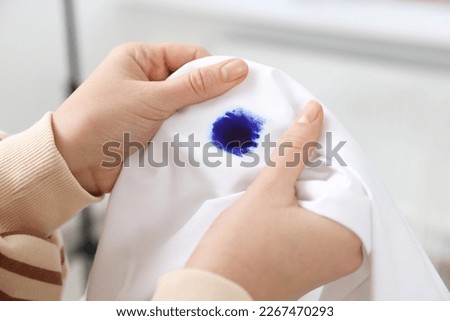 Woman holding white shirt with blue ink stain on blurred background, closeup Royalty-Free Stock Photo #2267470293