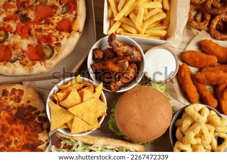 French fries, pizza and other fast food on wooden table, flat lay