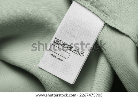 Clothing label on light green garment, top view Royalty-Free Stock Photo #2267475903