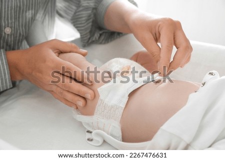 Mother cleaning navel of her baby with cotton bud on changing table, closeup Royalty-Free Stock Photo #2267476631