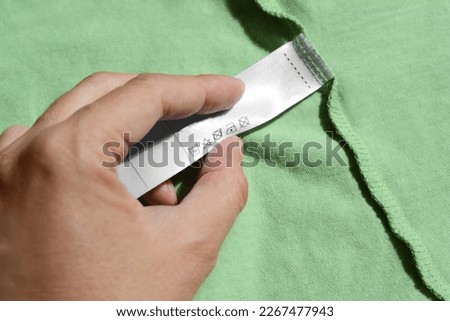 Woman holding clothing label on green garment, closeup