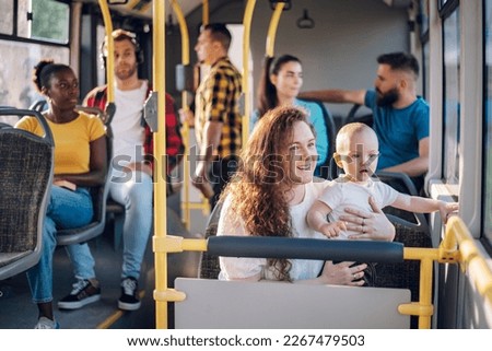 Young caring mother sitting with son in a bus while riding in a city. Boy is sitting in her lap and looking trough a window. Close up of plus size mom holding her child in public transportation. Royalty-Free Stock Photo #2267479503