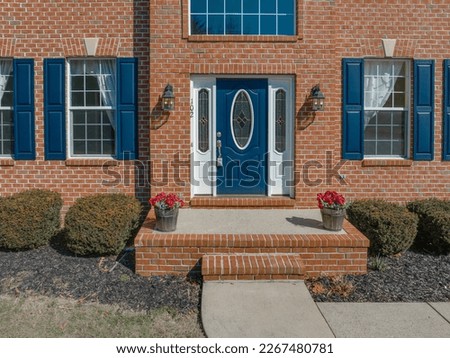 Close up view of elegant blue wooden door with oval stained window, with white sidelights, silver brass color door knob, iron wall light on red brick facade Royalty-Free Stock Photo #2267480781