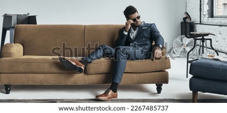 Handsome young man in nice suit adjusting his sunglasses while relaxing on the couch Royalty-Free Stock Photo #2267485737