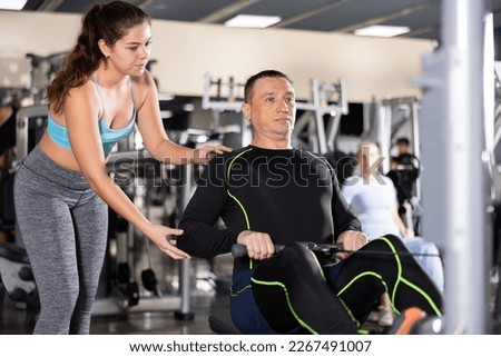 Focused young female trainer controlling adult man doing seated row on cable machine in gym during weight training for back muscles Royalty-Free Stock Photo #2267491007