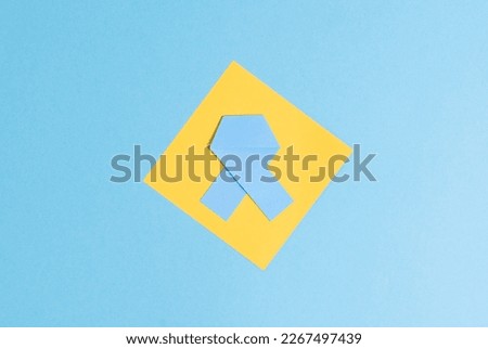 One blue paper ribbon with a sheet of paper lies in the center on a blue background, flat lay close-up. World Colon Cancer Day concept.