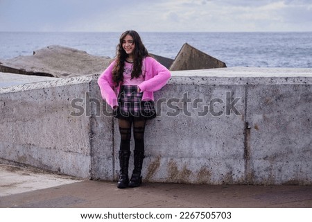Teenage girl wearing gothic pastel style in black and pink colours laughs while posing by the sea.