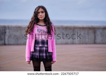 Profile portrait of pretty teenage girl posing dressed in gothic style in black and pink colours. Long black hair. Latin features.