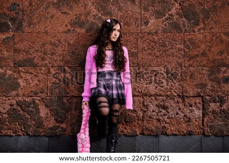 Teenager posing dressed in gothic style in black and pink colours with a melancholic look.