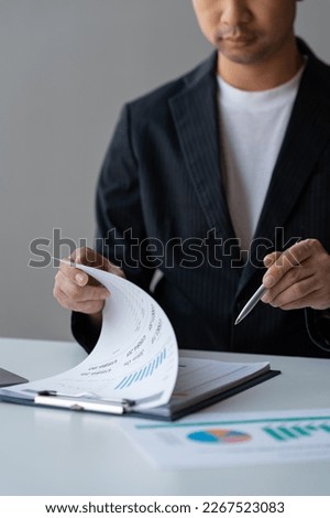 Young Asian businessman examining chart analyzing documents Financial data graph showing investment income in real estate business in office accounting management concept.
