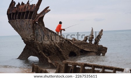An Angler Standing On A Sunken Shipwreck, On The Beach In Muntok Town In The Afternoon Royalty-Free Stock Photo #2267535611