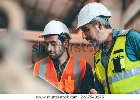 Teamwork men in construction site, Two civil engineer or professional foreman in safety helmet hard hat using blueprint in digital tablet working while standing at industrial factory, teamwork concept