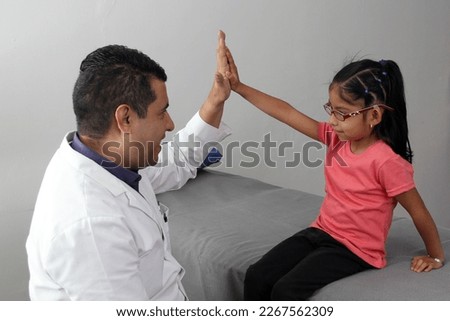 Pediatrician doctor and 4 year old latin girl patient in consultation are friends and make hi five sign and bump fists
