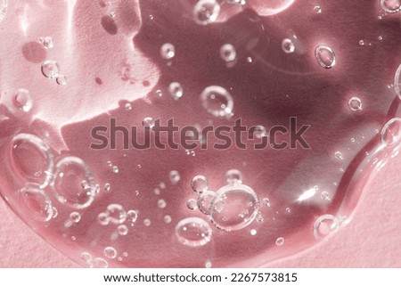 Transparent cosmetic liquid for skin care top view, macro. Liquid natural cleansing gel with peptides, acids and bubbles on a pink background, selective focus. Royalty-Free Stock Photo #2267573815