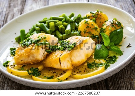 Fish dish - fried halibut with baked potatoes and boiled green beans on wooden table 