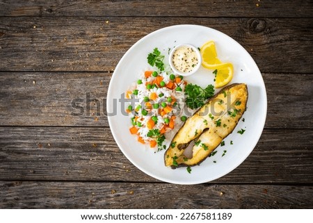 Fish dish - fried halibut with white rice, peas and carrots on wooden table 
