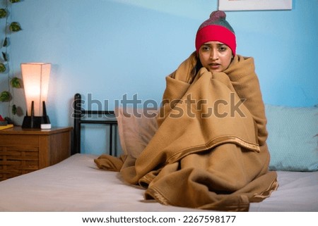 shivering Young girl full coverd with blanket and cap sitting on bed at during night - concept of chilling winter cold, climate change and influenza or fever Royalty-Free Stock Photo #2267598177