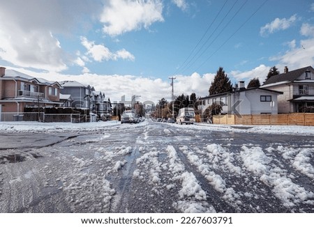 Slushy residential street after snow storm or arctic blast. Sunny day with big melt down on unplowed side street with parked cars. East Vancouver with skyline of downtown Vancouver. Selective focus.