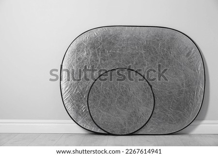 Studio reflectors near grey wall in room, space for text. Professional photographer's equipment