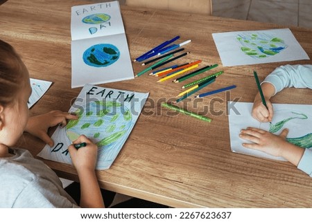 Children draw the planet Earth with pencils and felt-tip pens on album sheets for Earth Day at their home table. The concept of protecting the environment, peace on Earth. Royalty-Free Stock Photo #2267623637