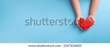Hands of little girl child holding heart made of plastic bricks on blue background
