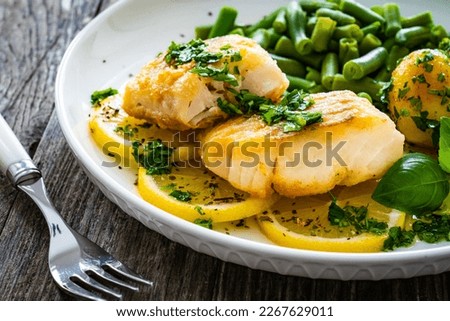 Fish dish - fried halibut with baked potatoes and boiled green beans on wooden table 