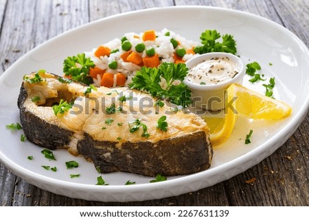 Fish dish - fried halibut with white rice, peas and carrots on wooden table 