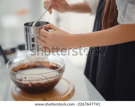 DIY home cooking concept. brunette woman sifting flour for cake through sieve, salting dough. Young woman smiling, loves to cook in beautiful modern kitchen.