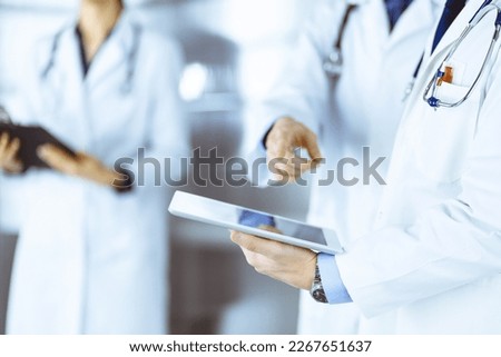 Group of unknown doctors use a computer tablet to check up some medical names records, while standing in a hospital office. Physicians ready to examine and help patients