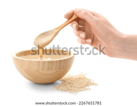 Female hand with bowl of tasty tahini and sesame seeds on white background, closeup Royalty-Free Stock Photo #2267651781