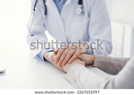 Doctor and patient sitting at the table in clinic office. The focus is on female physician's hands reassuring woman, only hands close up. Medicine concept. Royalty-Free Stock Photo #2267652997