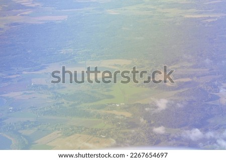 Aerial view of green and yellow fields, forests, nature and some small white clouds. View from an airplane window of rural countryside area, in the air. Rainbow color effect on the photo.
