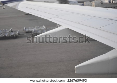 Close-up of an airplane wing pictured from inside the aircraft. Plane landing or waiting to leave ground on the airport during morning or daytime. 