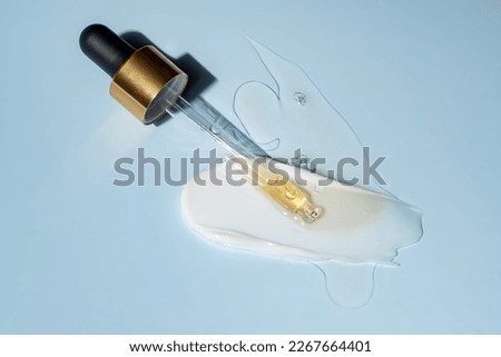 Cosmetic dropper with yellow oil and pace cream smear. Anti-aging cosmetics on blue background Royalty-Free Stock Photo #2267664401