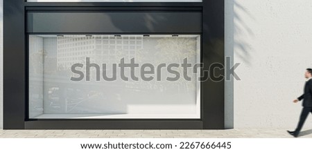 Man walking by sunlit wall background with place for your advertising poster near empty shop window with space for your product presentation in modern building area outdoors, mock up Royalty-Free Stock Photo #2267666445