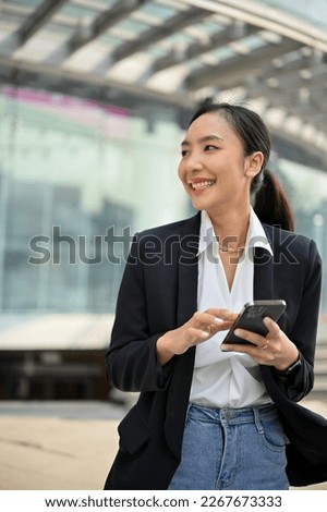 Portrait, Attractive and confident millennial Asian businesswoman in casual suit using her smartphone at outside of the company building. Royalty-Free Stock Photo #2267673333